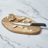 A wooden cutting board on a marble surface holds a garlic bulb, garlic cloves, garlic slices, and a paring knife with a black handle.