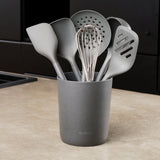 A gray Zyliss 7-Piece Utensil Set with ergonomic handles rests on the counter, holding spatulas, a slotted spoon, whisk, and ladle—all in heat-resistant gray PBT.