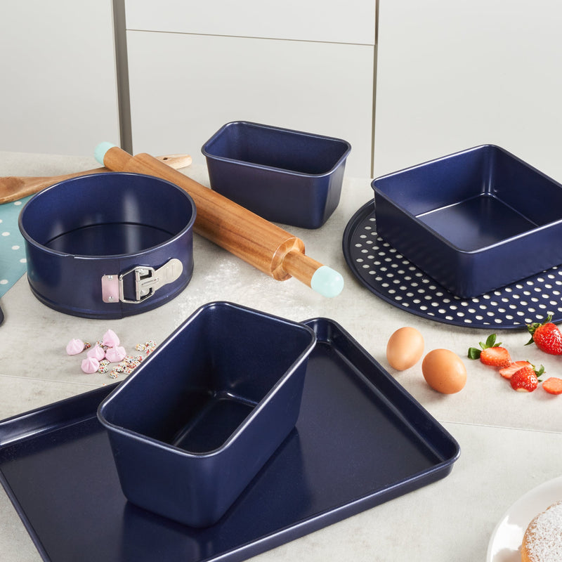 A kitchen counter is set with a Zyliss Durable Non-Stick Removable Base Cake Pan among other blue nonstick bakeware, including a rolling pin, trays, springform and loaf pans, eggs, strawberries, a whisk, and baking essentials. #20cm/8"