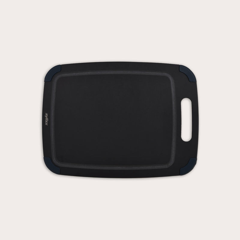 The Zyliss Wood Fibre Cutting Board is a rectangular, black, eco-friendly board with rounded corners, groove edging, right-side handle cutout, and dark blue corner accents. Made from recycled wood fibres. Shown on a plain white background. #Medium