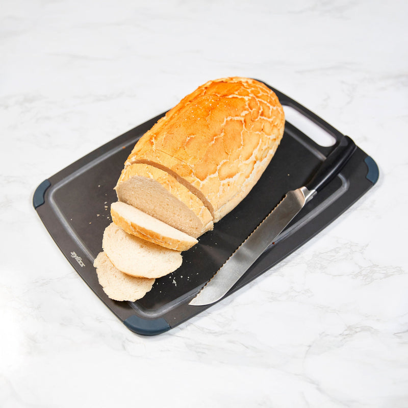A partially sliced loaf of bread and a bread knife rest on a Zyliss Wood Fibre Cutting Board atop a white marble surface. #Large