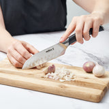 A person chops garlic on a wooden cutting board using the Zyliss Comfort Pro Mini Santoku Knife 13cm / 5 with an ergonomic handle; two whole shallots rest nearby on a white countertop.