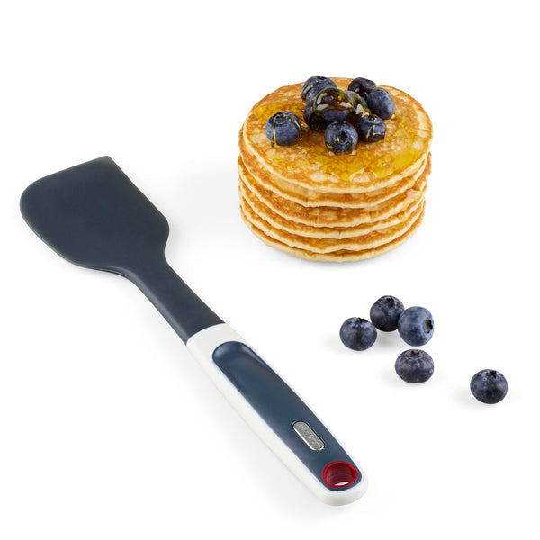 A stack of pancakes topped with blueberries and syrup sits beside a few loose blueberries and the Zyliss Does it All Silicone Spatula, featuring a heat-resistant and ergonomic design, on a white background.