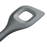 A close-up of a gray kitchen utensil with a flat, angled head and a large square hole in the center, designed for stirring or serving food.