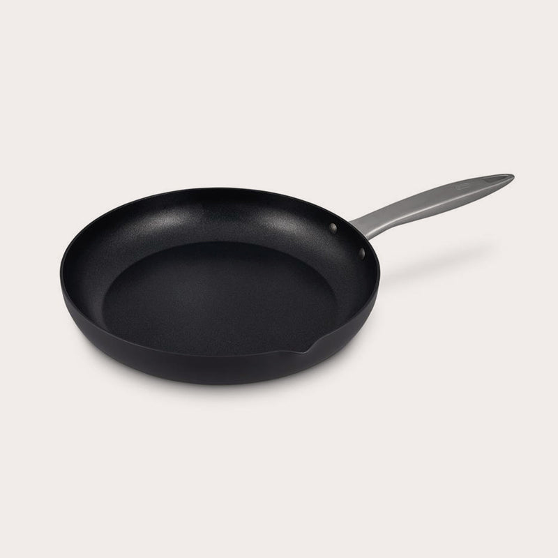 The Zyliss Ultimate Pro Non-Stick Frying Pan With Pouring Lip, crafted from hard-anodized aluminium with a shiny silver handle, features gently sloped sides, a Swiss-engineered coating, and a small pouring spout on one edge. #28cm/11"
