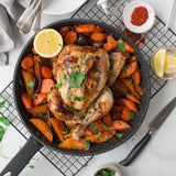 A roasted whole chicken garnished with fresh herbs sits in the Zyliss Ultimate Non-Stick Frying Pan, surrounded by carrots and potatoes. Half a lemon rests on top, with seasonings, lemon wedges, and cutlery nearby on a white table. #28cm/11"